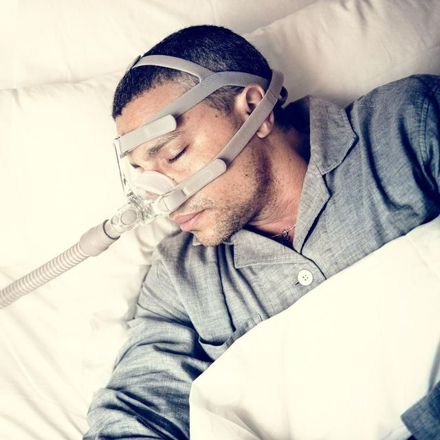 A man wearing a cpap mask is sleeping in a bed
