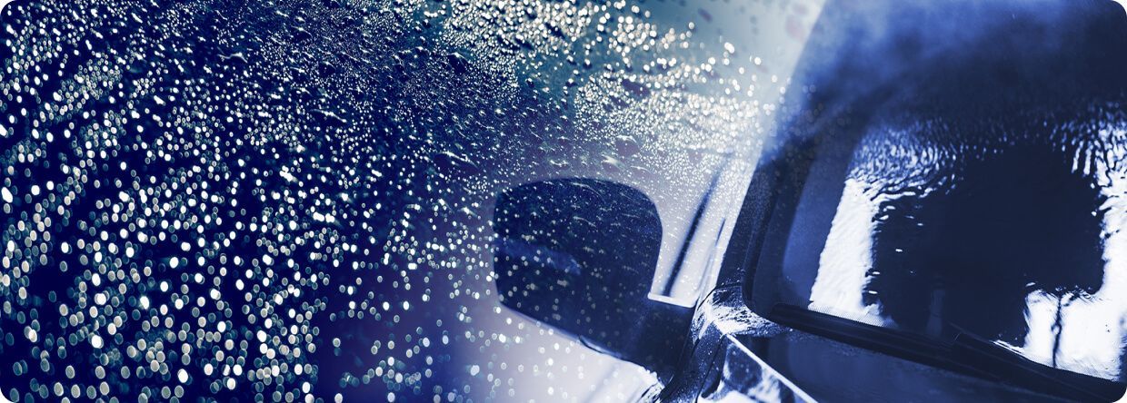 Car in heavy rain, dark blue hues, droplets on the window, blurred background.