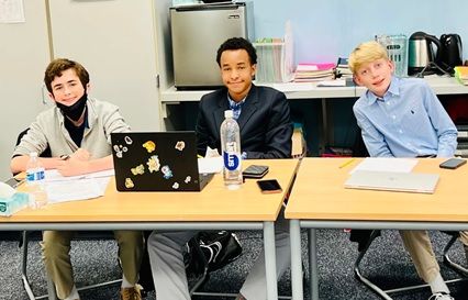 Three young men are sitting at a table with laptops.