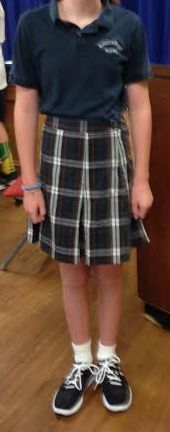 A person wearing a plaid skirt and a polo shirt is standing on a wooden floor.