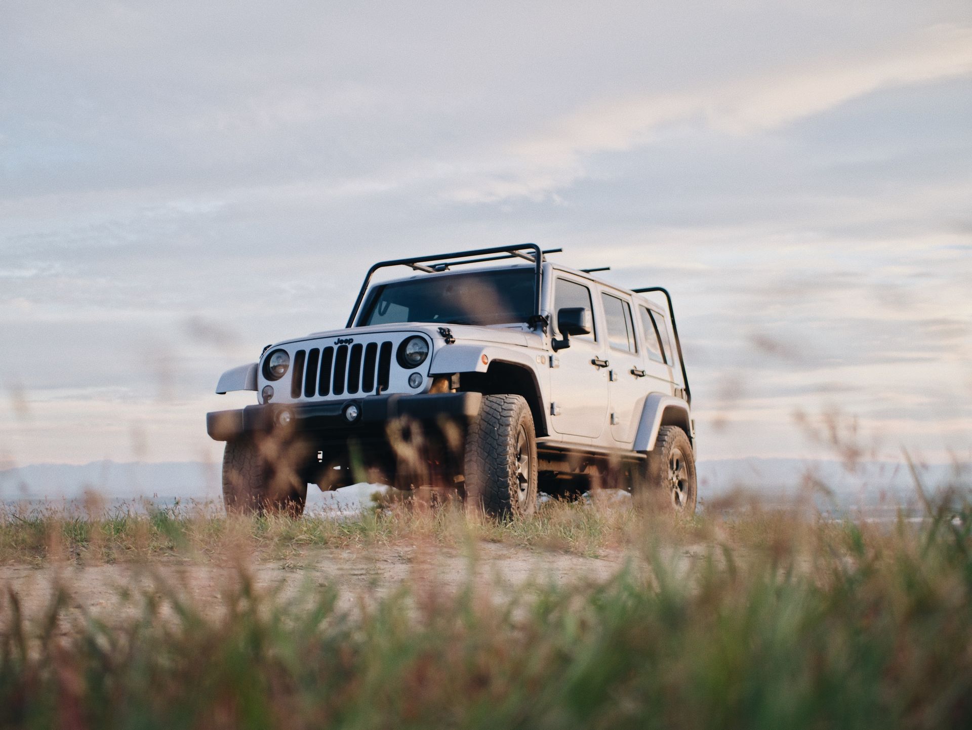 A white jeep is parked in a field of tall grass.