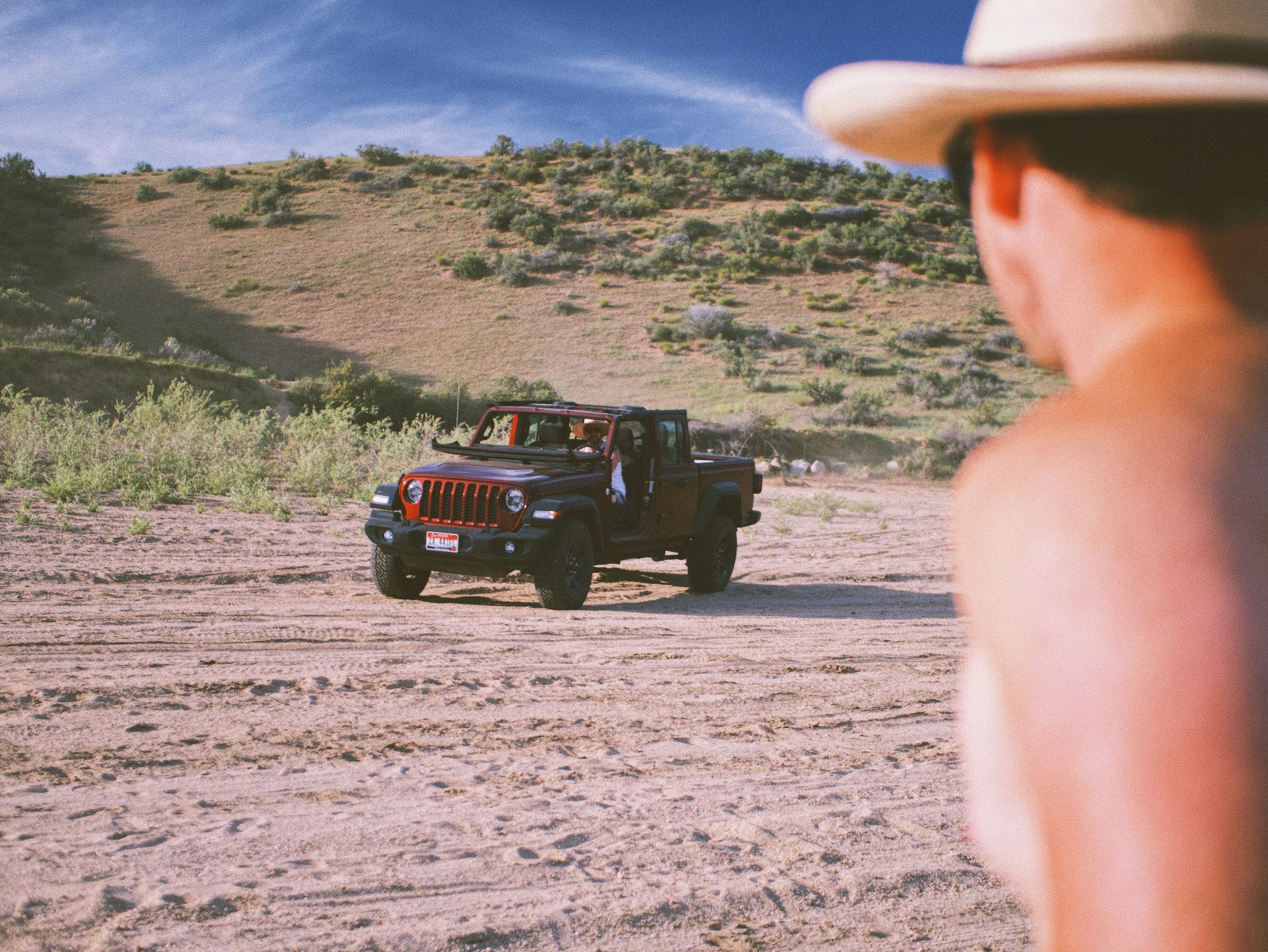 A man in a cowboy hat is looking at a jeep in the desert.