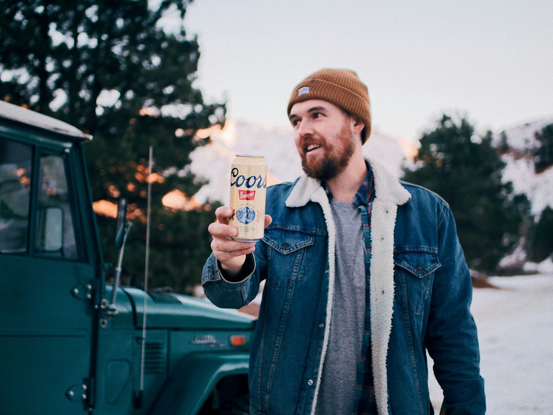 A man in a denim jacket is holding a can of beer.
