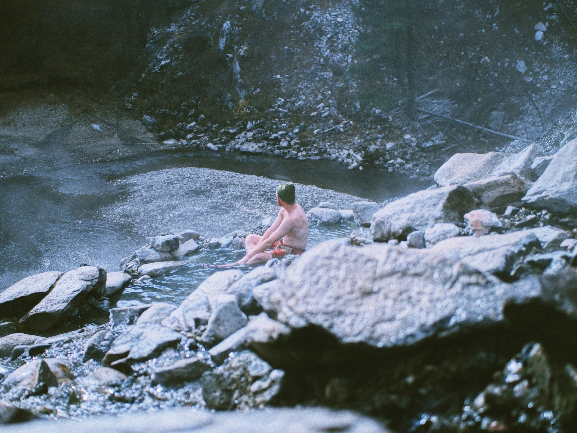 A man is sitting on a rock in a river.