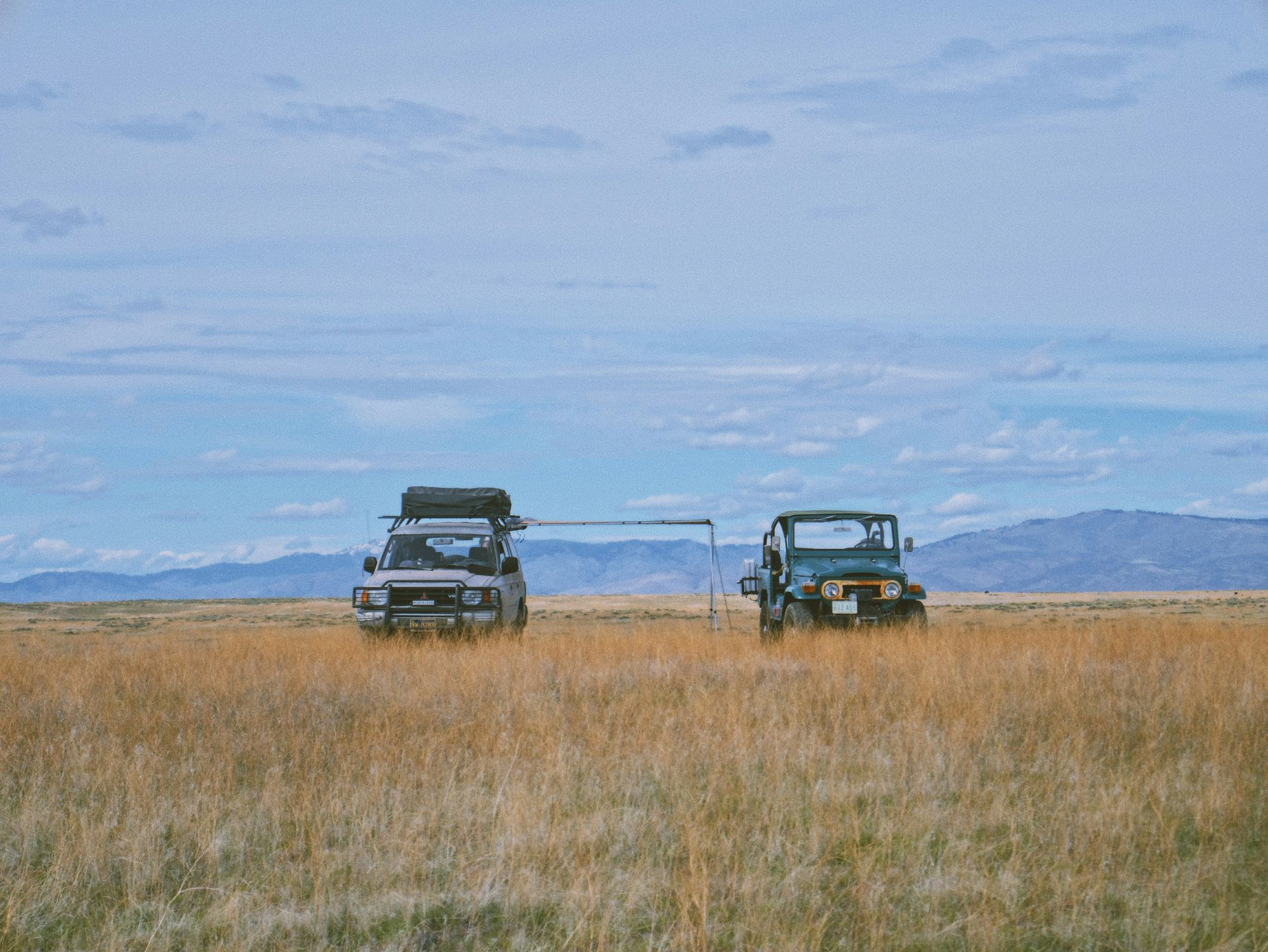 Two cars are parked in a field with mountains in the background.