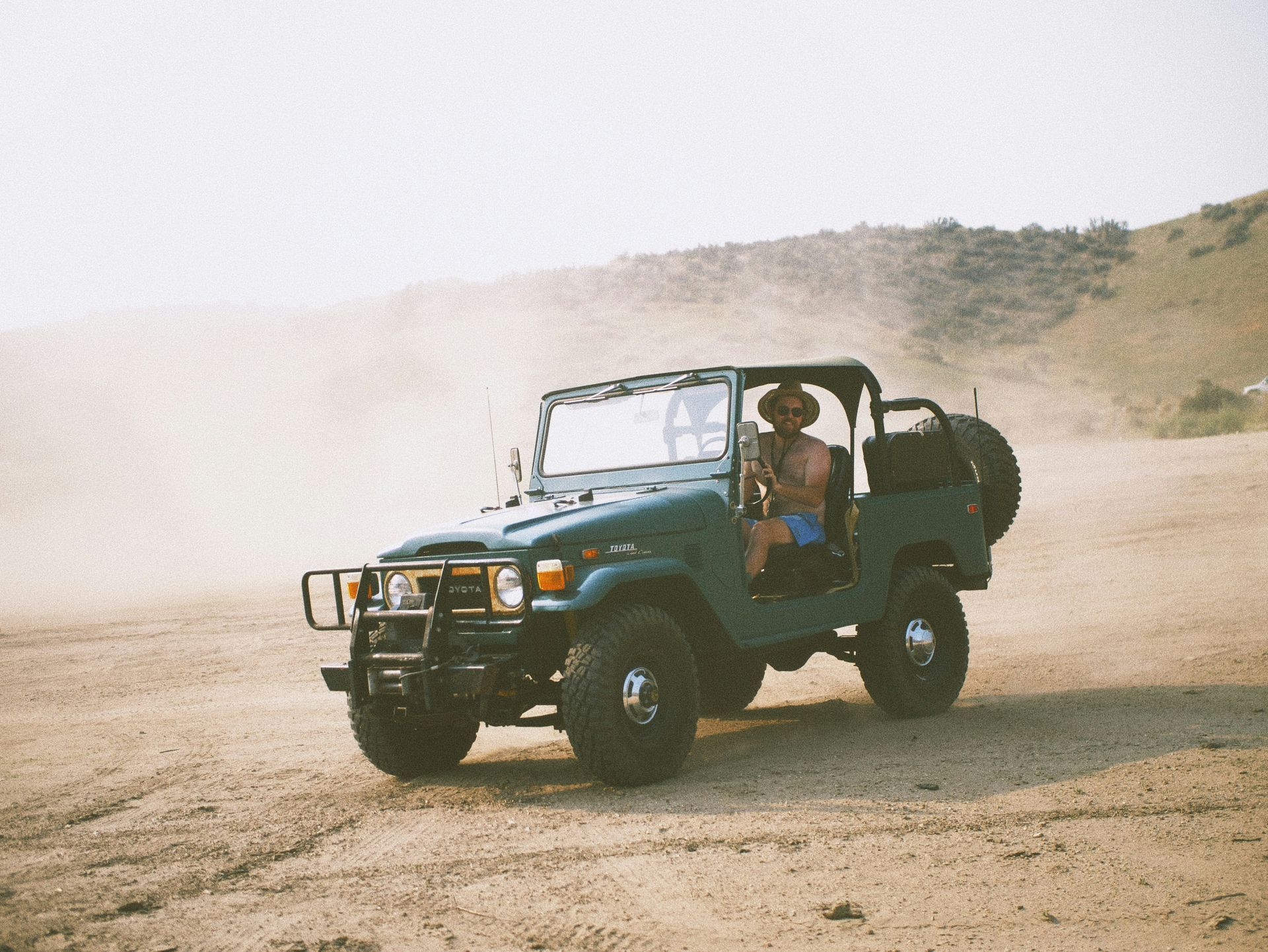 A man in a cowboy hat is driving a jeep on a dirt road.