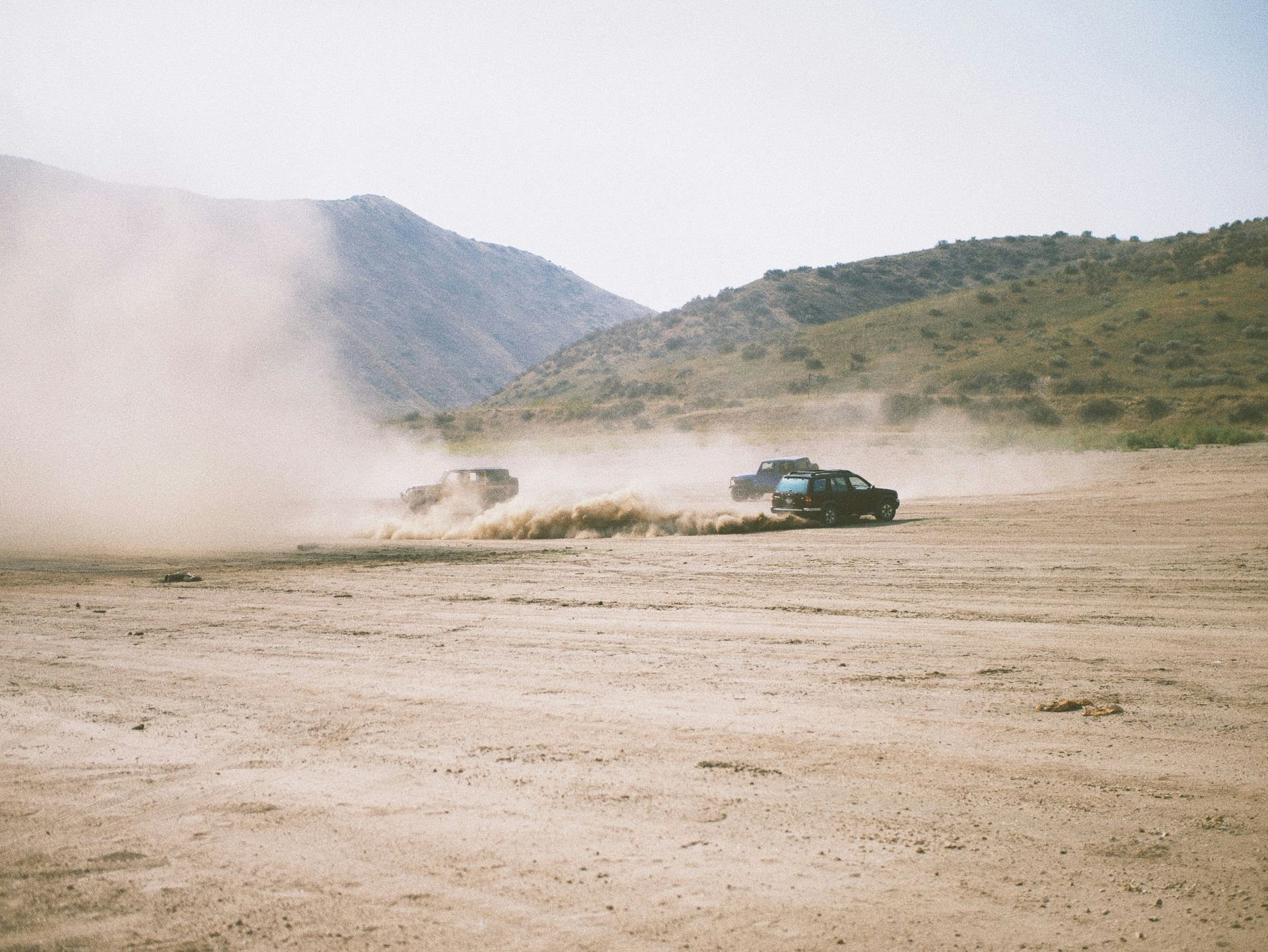 A truck is driving through a dirt field with mountains in the background