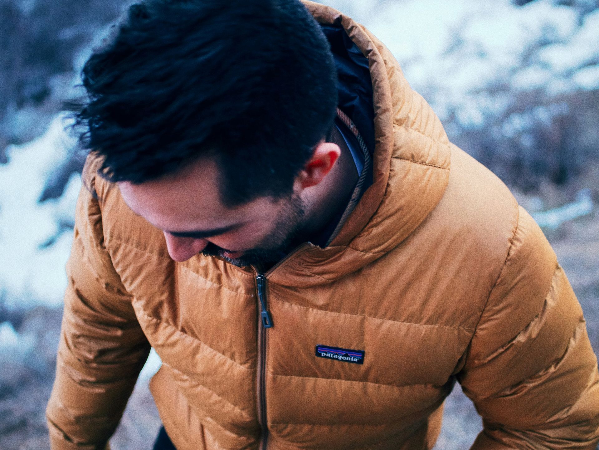 A man wearing a patagonia jacket with a hood is looking down.