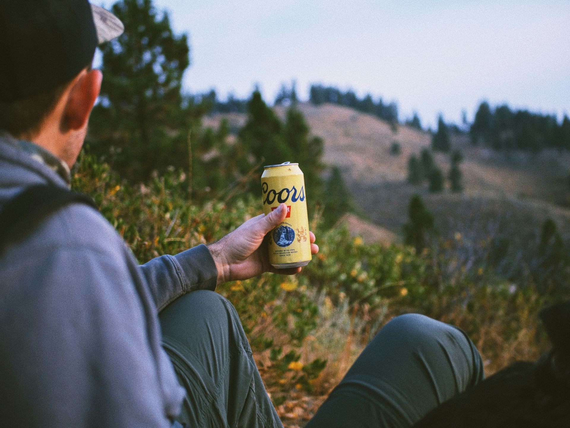 A man is sitting on a hill holding a can of beer.