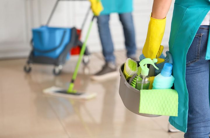 Person holding cleaning supplies, another mopping floor, in a bright room.