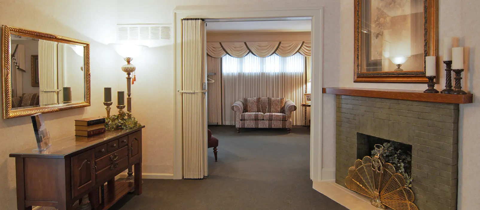 Interior view of a funeral home with a fireplace, antique furniture, and a hallway leading to a seating area.