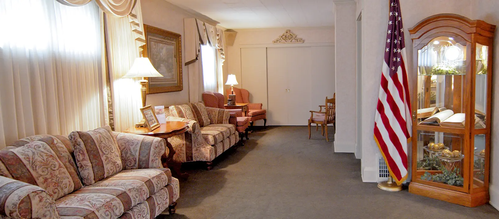 A formal living room with couches, an American flag, and display cabinet.