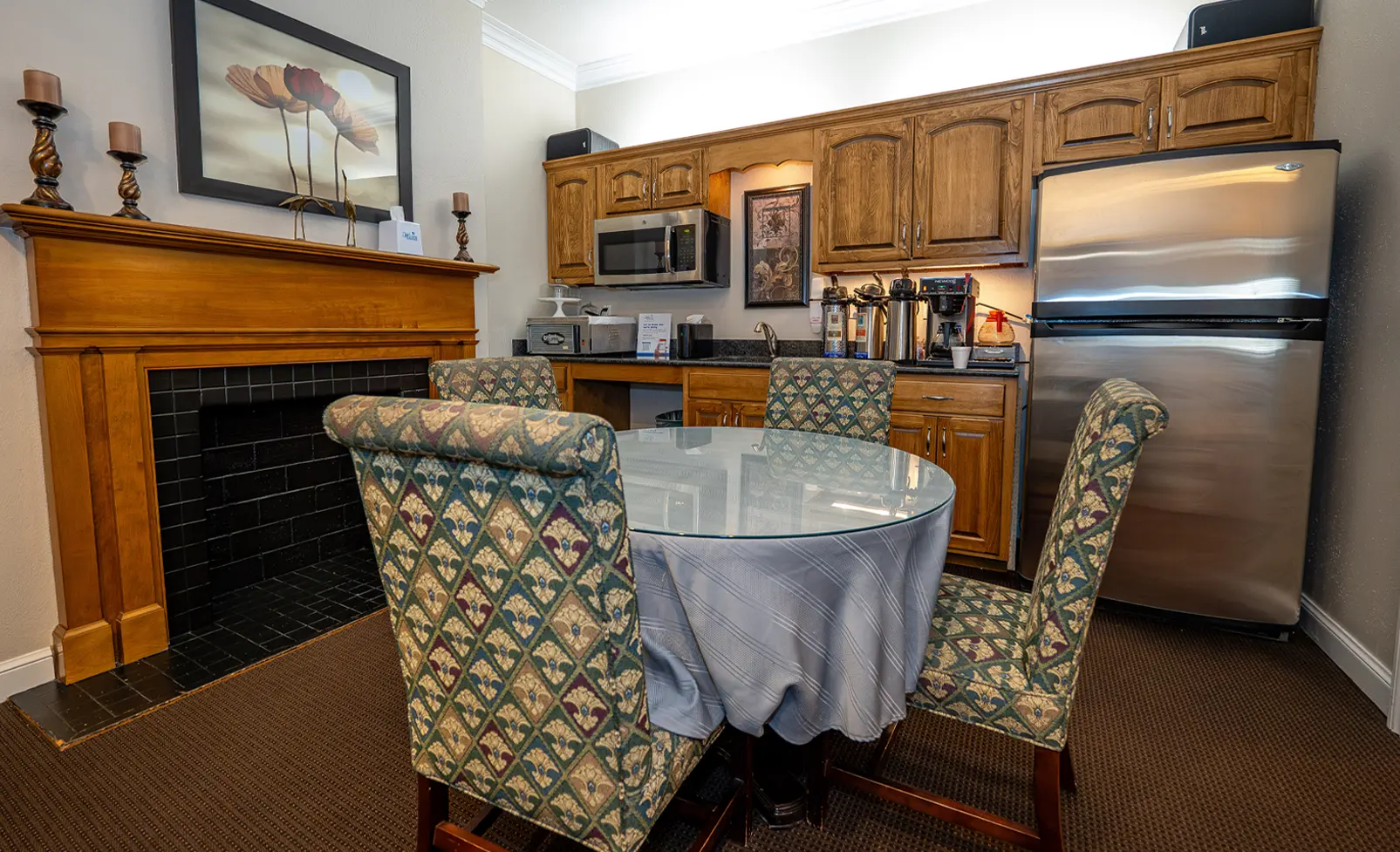 Dining area with fireplace, kitchen cabinets, round table, chairs, and stainless steel refrigerator.