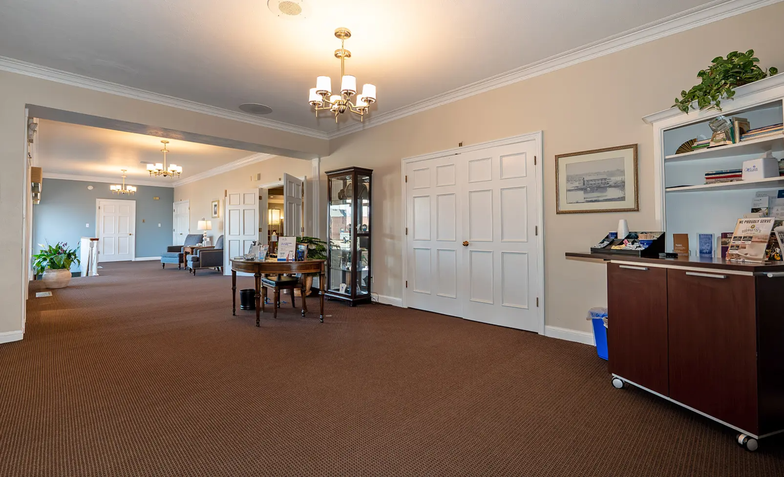 Large, carpeted lobby with furniture, including a reception desk and display case, and a pair of double doors.