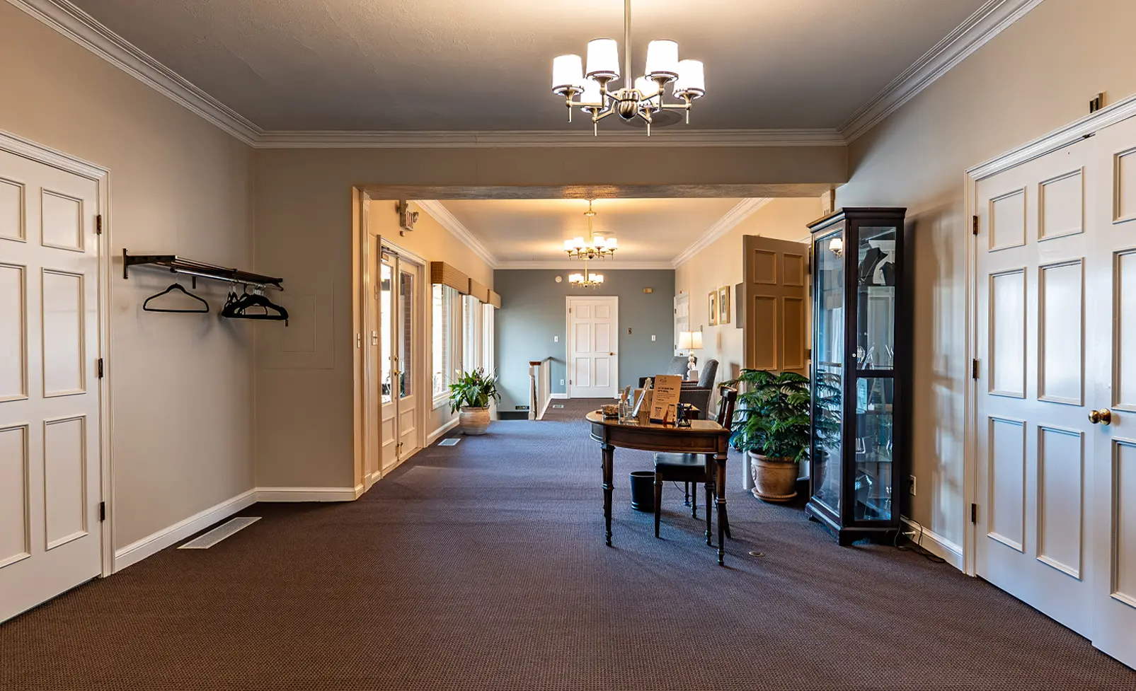 Hallway with brown carpet, white doors, and a table; chandelier overhead.