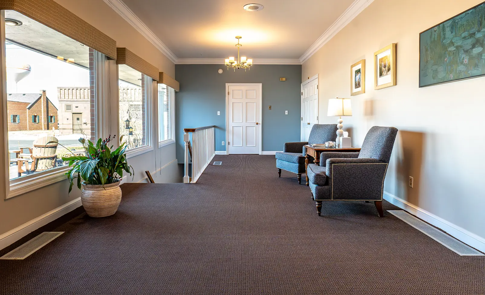 Hallway with carpet, blue walls, two armchairs, large windows, and a white door.