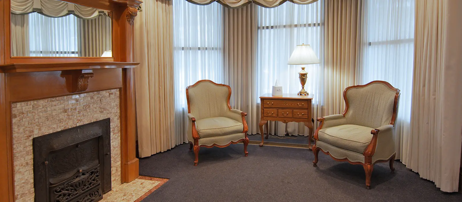 A cozy room with a fireplace, two armchairs, and a lamp next to a window.
