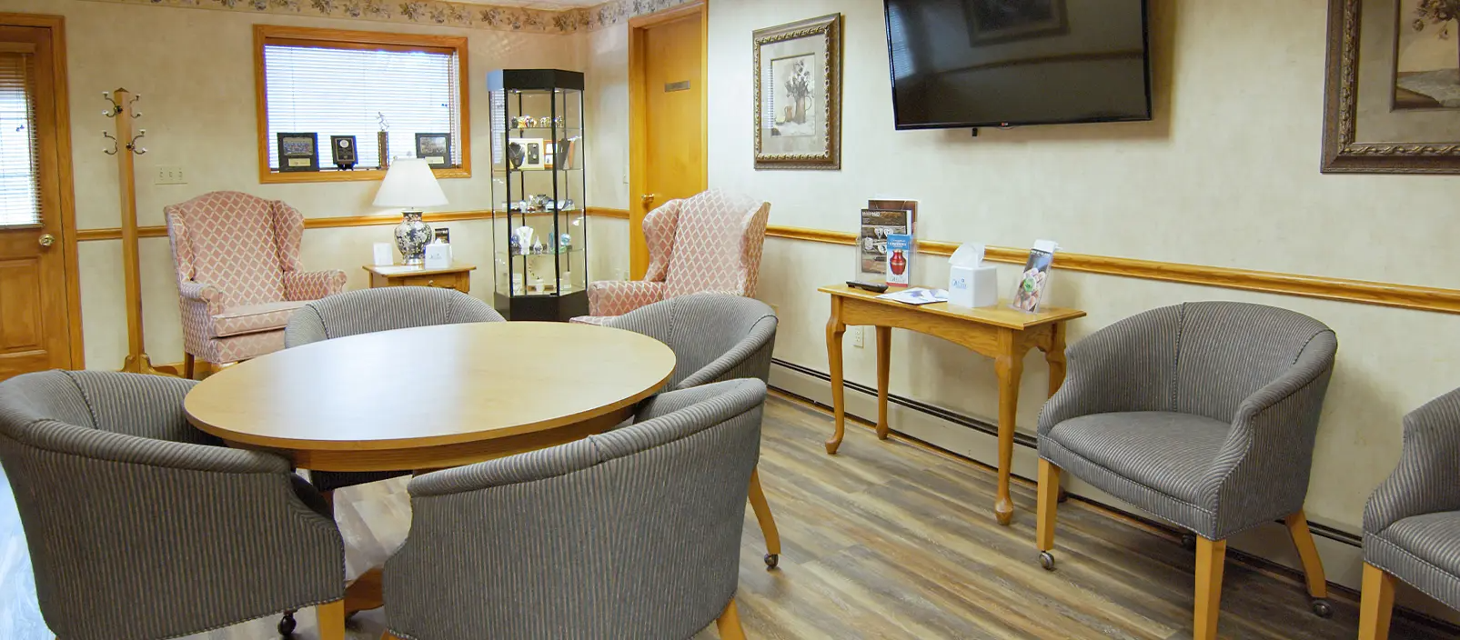 A waiting room with chairs around a table, and a TV on the wall.