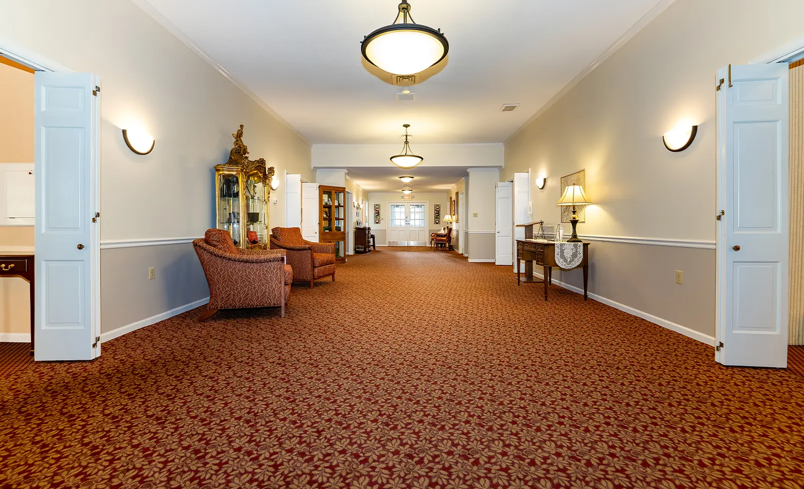 Long hallway with patterned red carpet and seating.