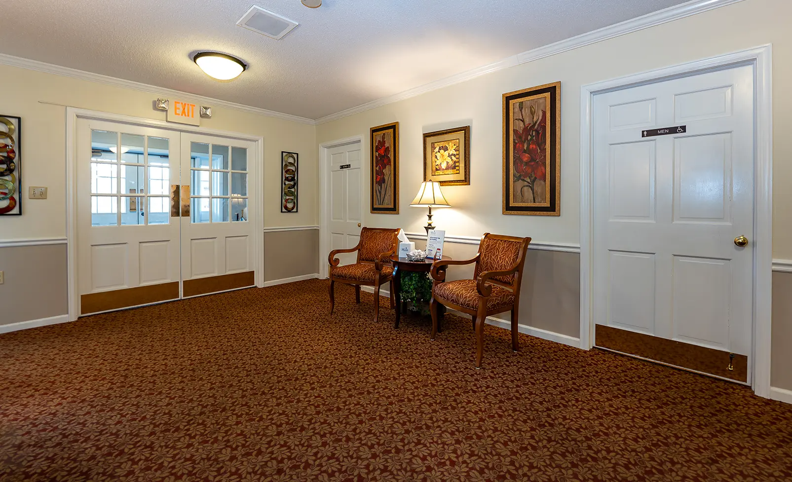 Hallway with two chairs, framed art, and double doors with carpet and white walls.