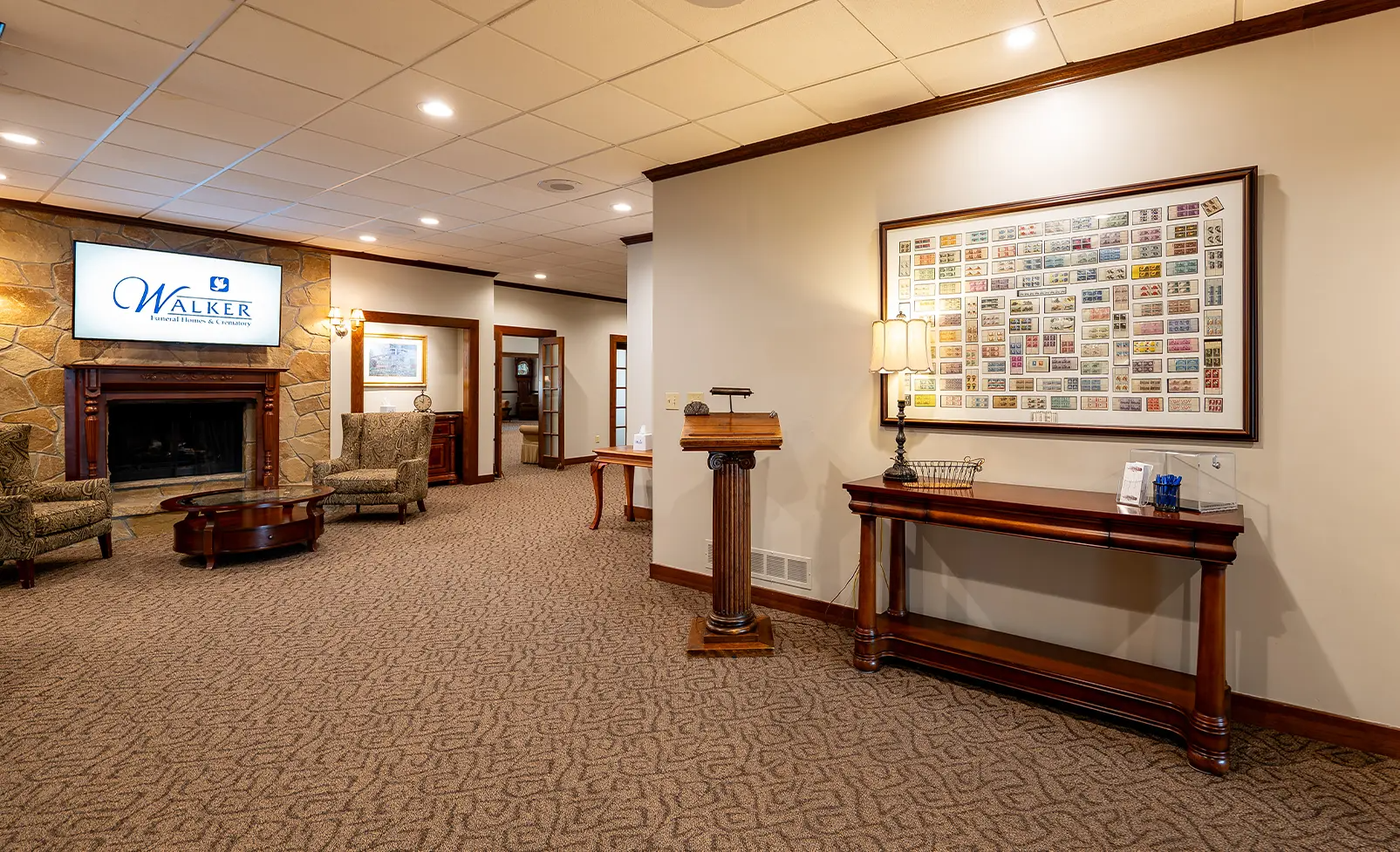 A lobby with a fireplace, seating, and a display case. Brown walls and carpet.