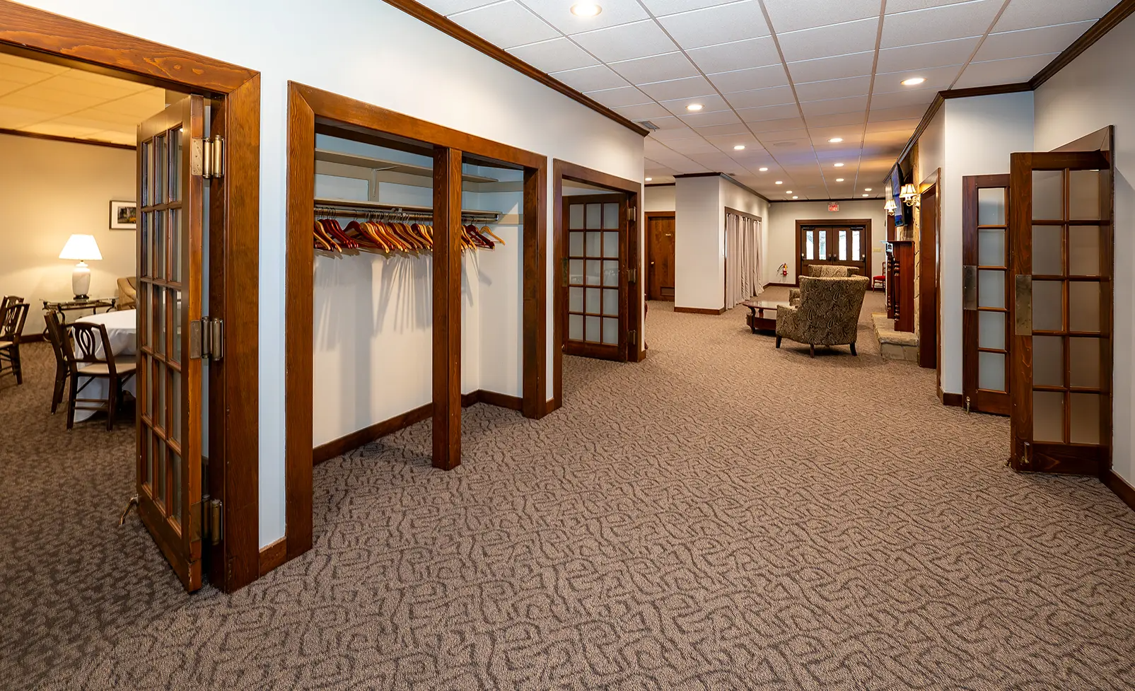 Room with open doors, coat racks, seating area. Brown carpet, white walls, wooden trim.