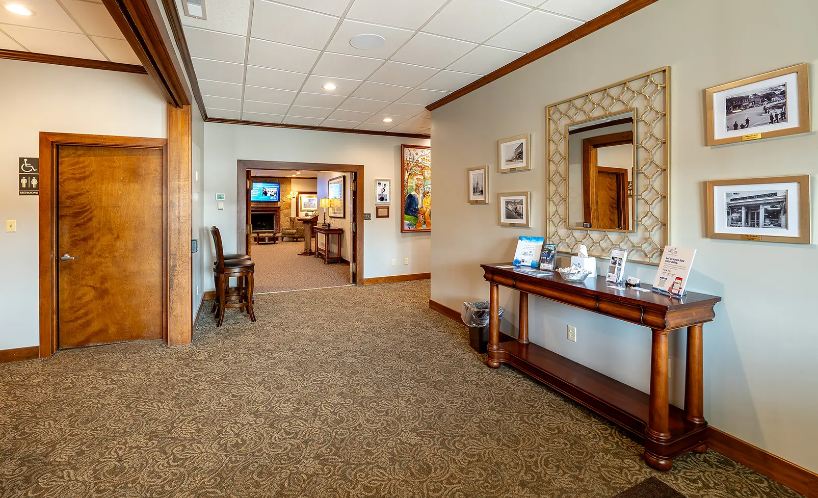 Hallway with brown carpet, wooden console table with mirror, doors to other rooms, photos on the wall.