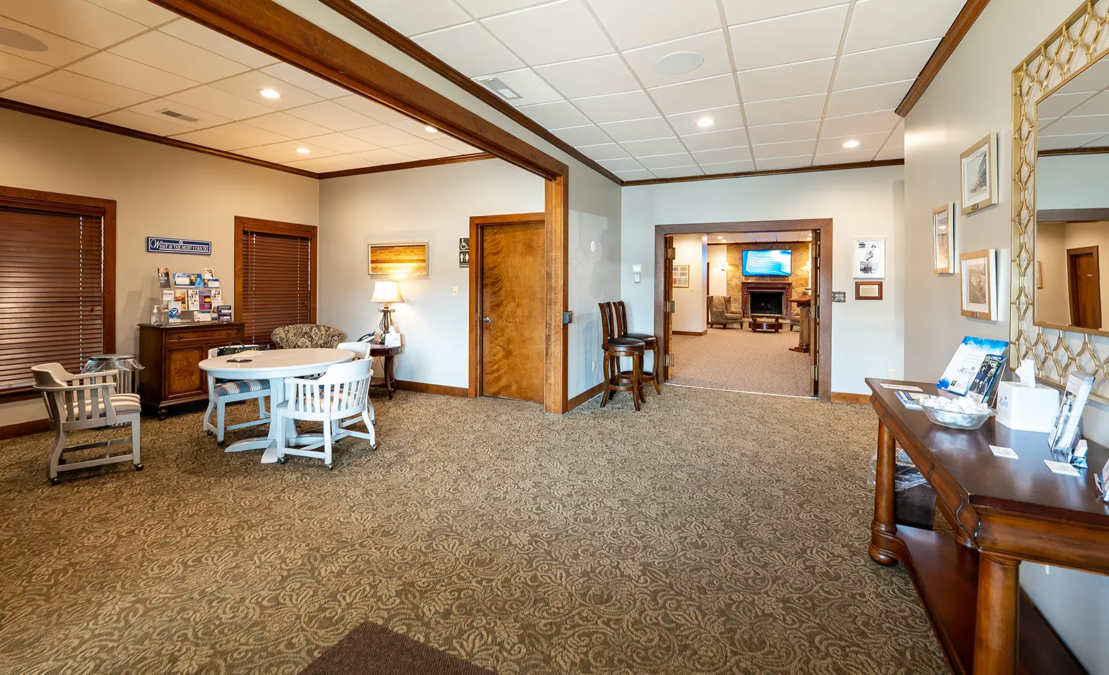 Interior view of a room with a table, chairs, and an open doorway to a fireplace. Carpeted floor, neutral colors.