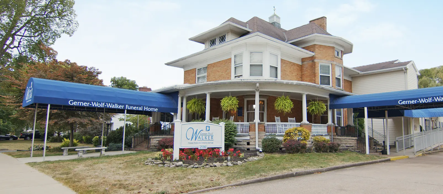 Historic brick building with blue awnings, a porch, and a sign in front of a grassy yard.