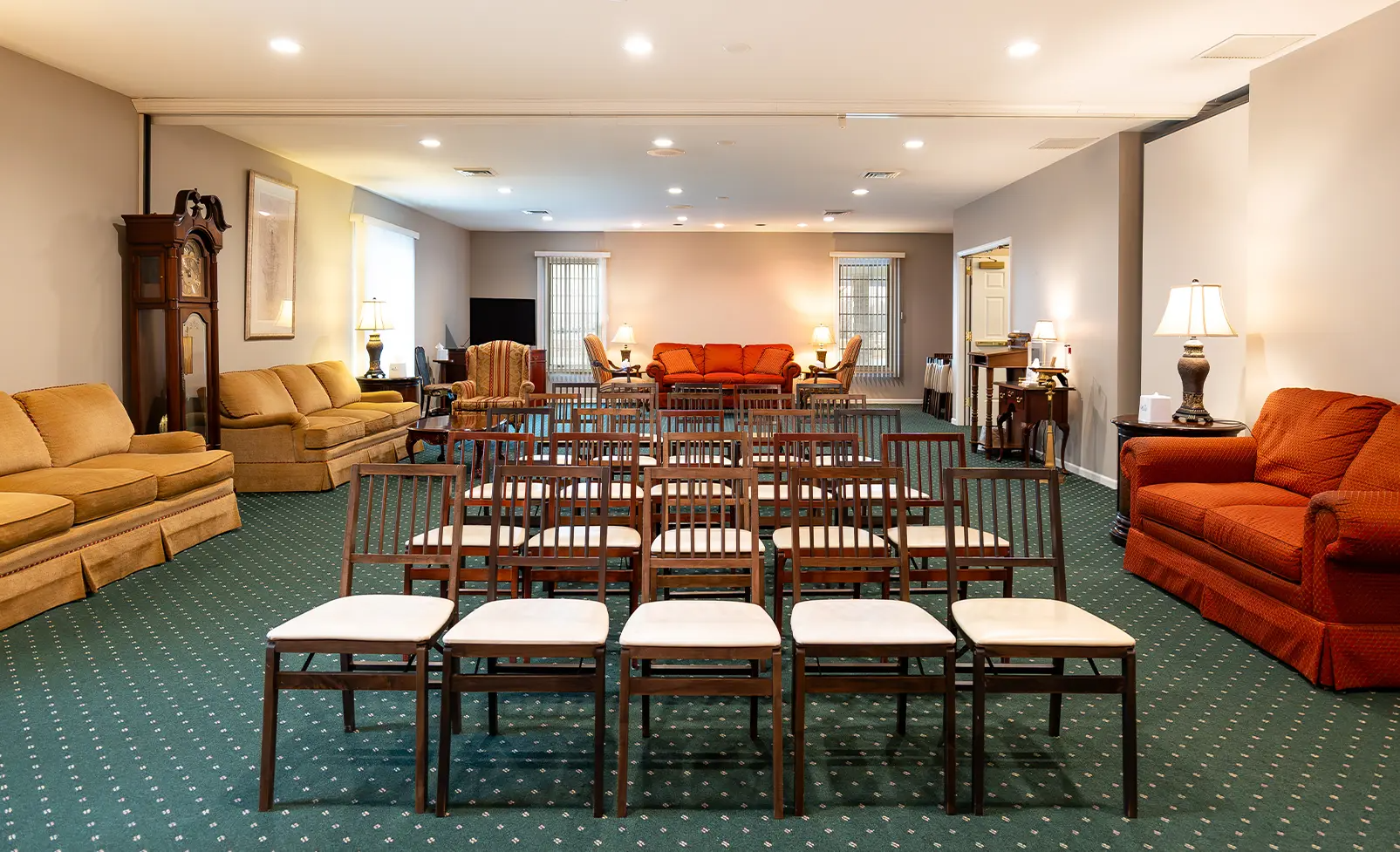A room with chairs arranged for a service, couches, and a grandfather clock.