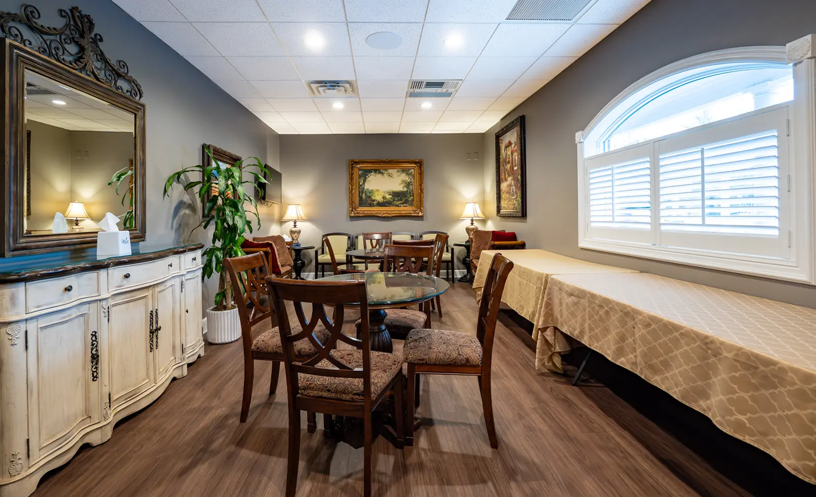 Elegant room with seating, large mirror, and a window with shutters; neutral colors, warm lighting.