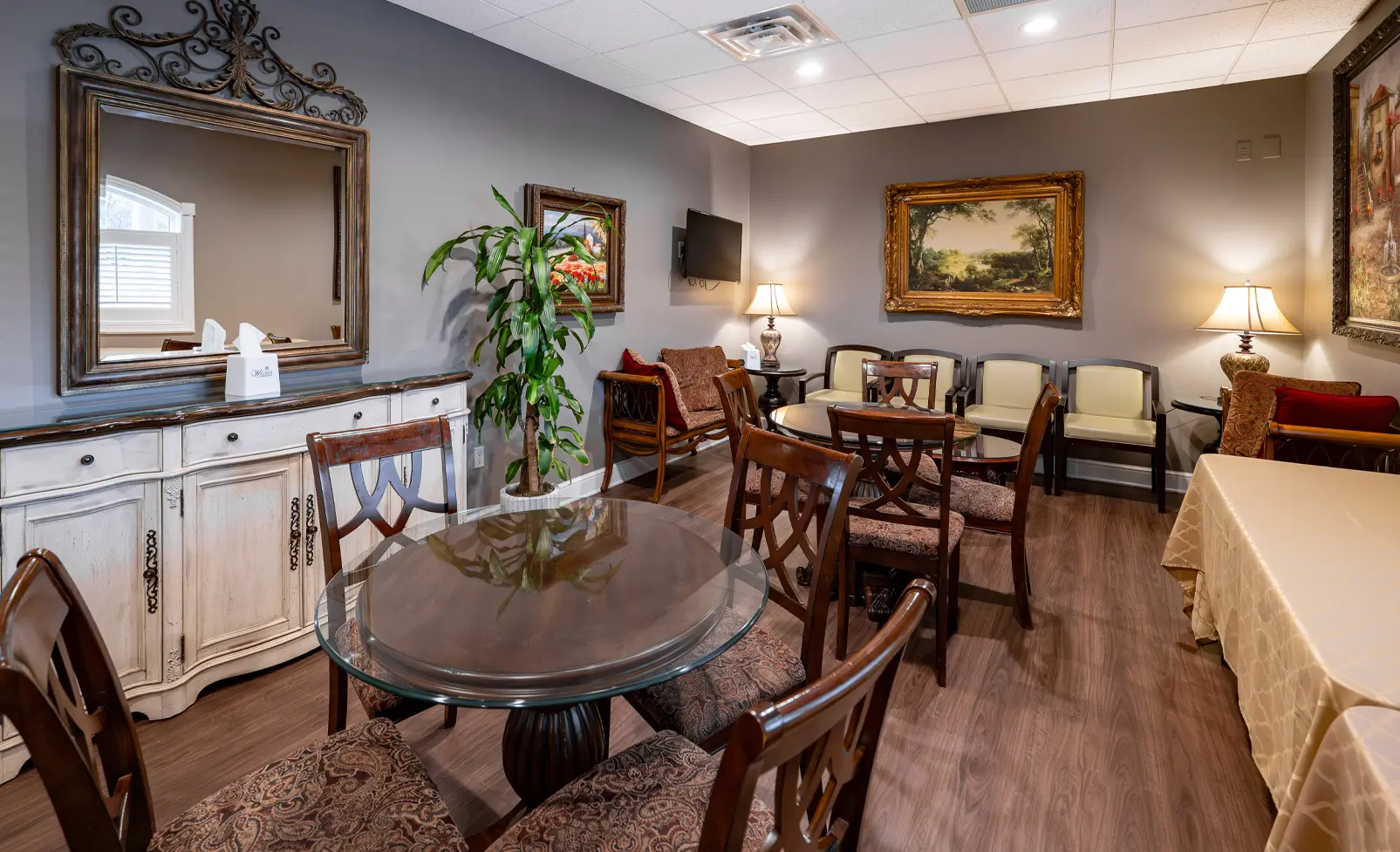 Waiting room with tables, chairs, antique furniture, artwork, and a large mirror.