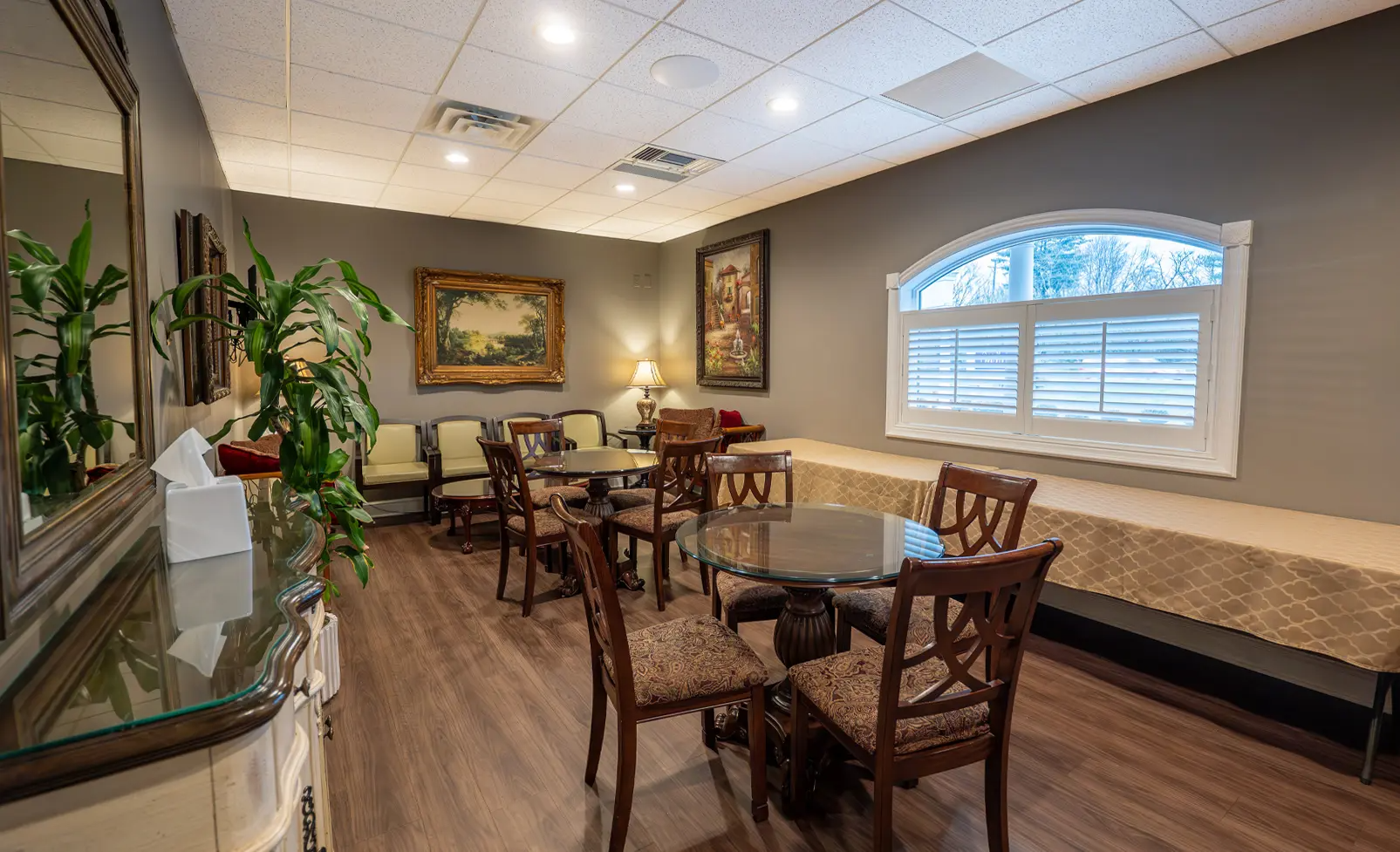 A waiting room with tables, chairs, artwork, a window, and a long table.