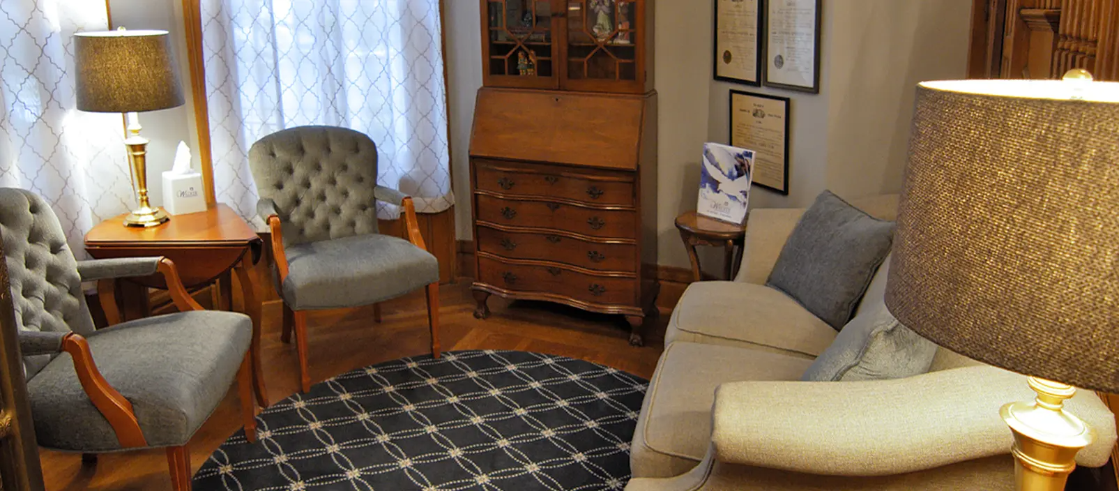 A cozy, well-lit room with antique furniture, a sofa, and two armchairs, with a patterned rug.