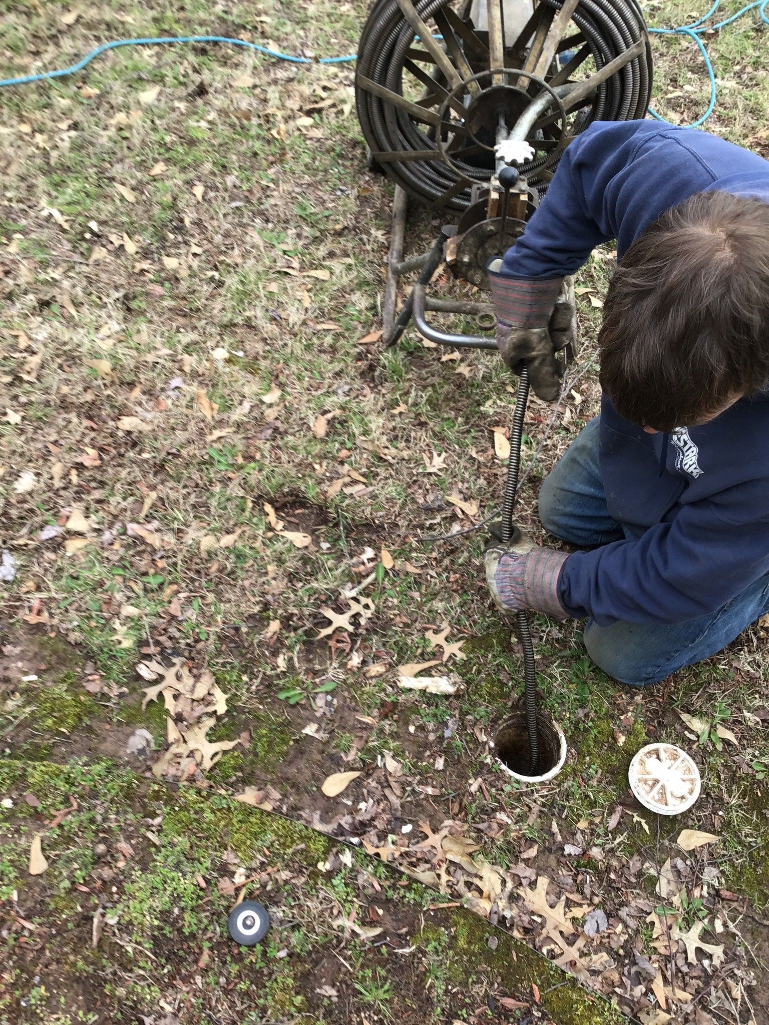 A man is kneeling down in the grass holding a hose.