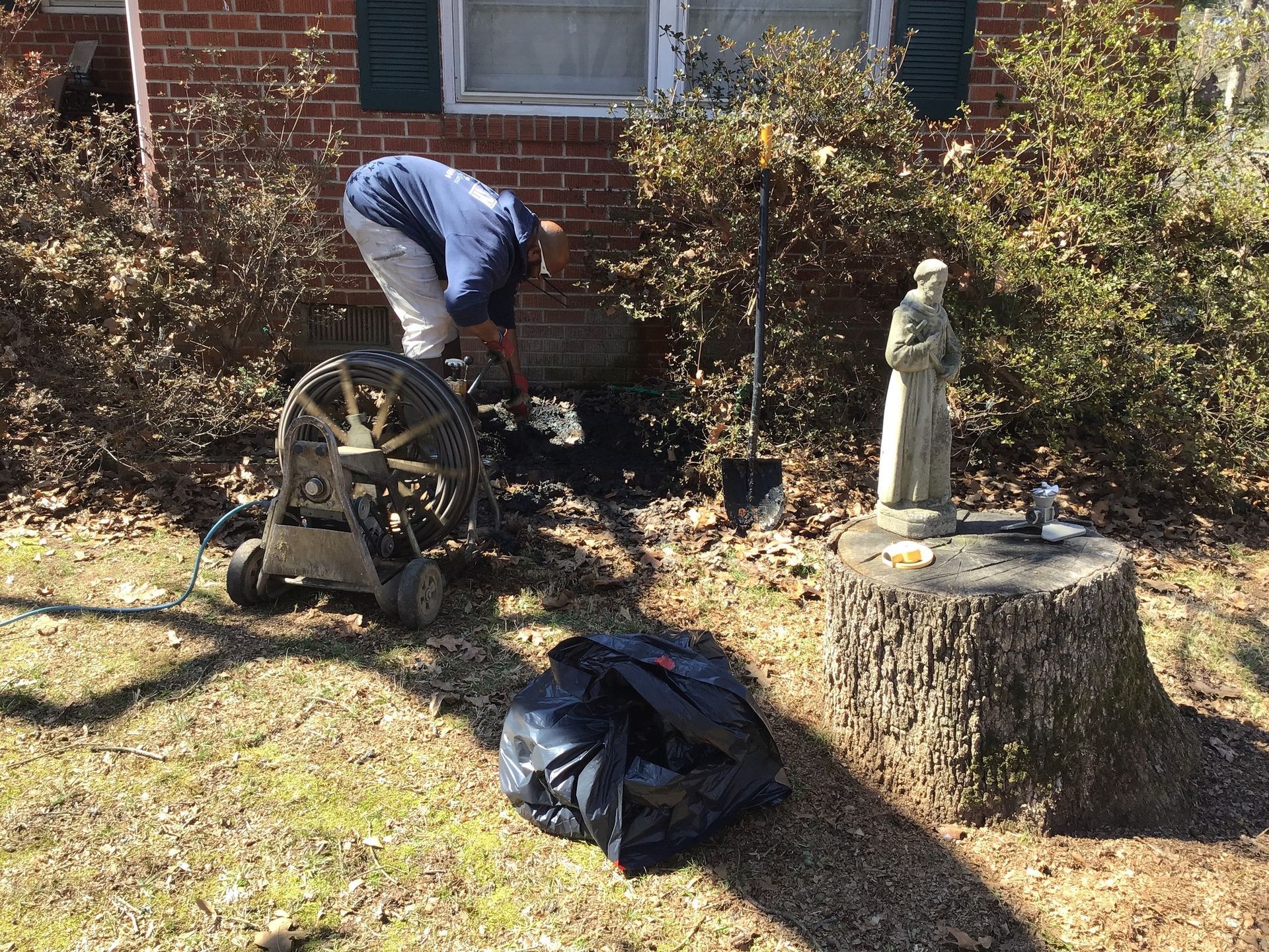A man is working on a drain in front of a brick house.