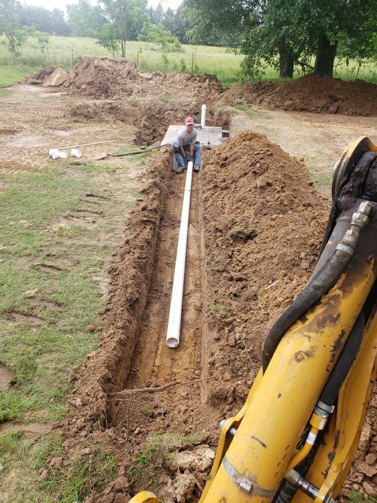 A man is sitting in the dirt next to a yellow excavator.