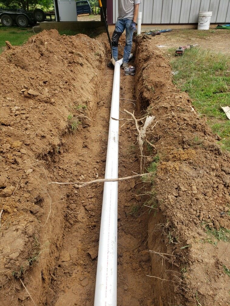 A man is standing next to a white pipe in the dirt.