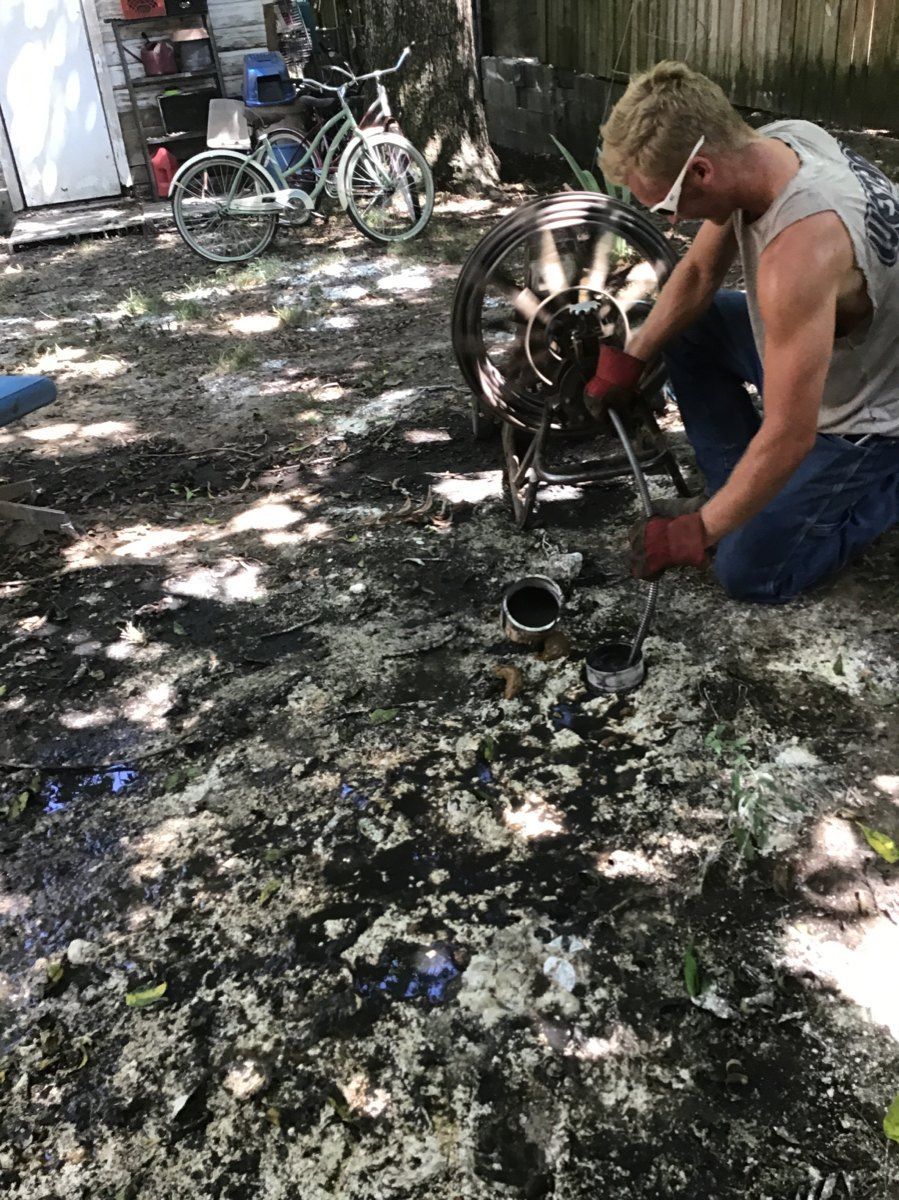 A man is kneeling down in the dirt working on a pipe.