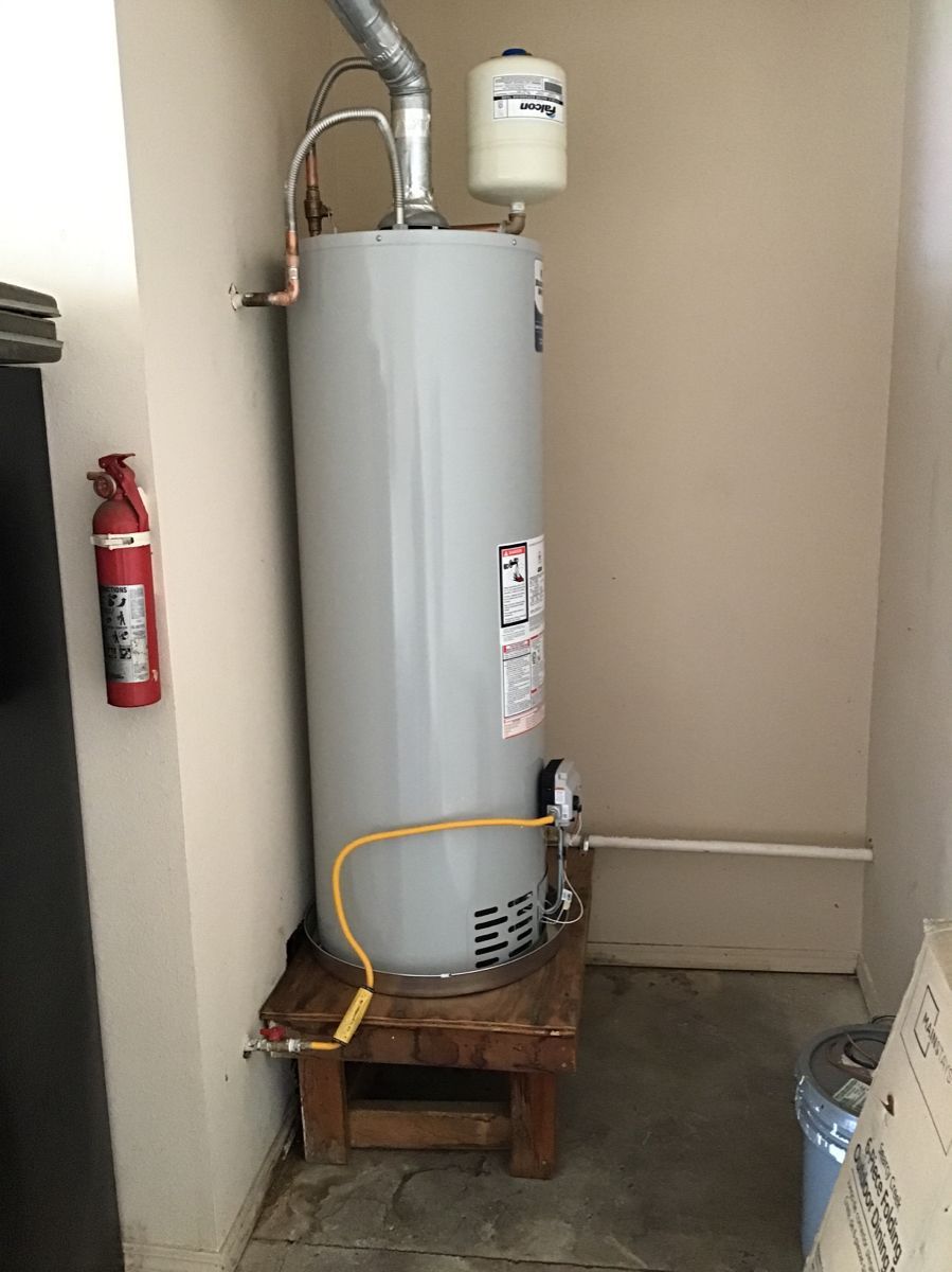 A water heater is sitting on a wooden stand in a room next to a fire extinguisher.