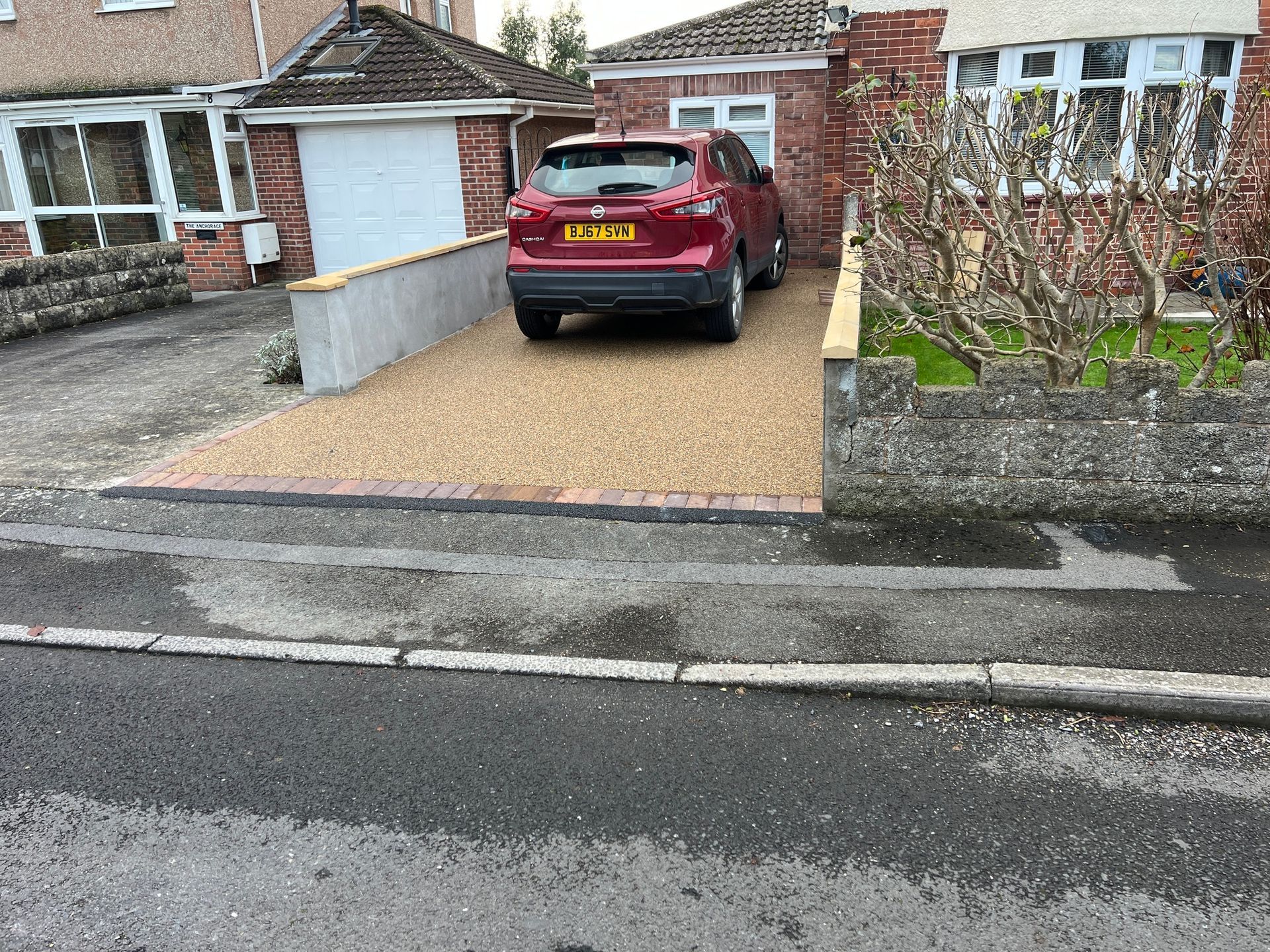 A red car parked on a freshly installed oat coloured resin driveway, with a house either side.