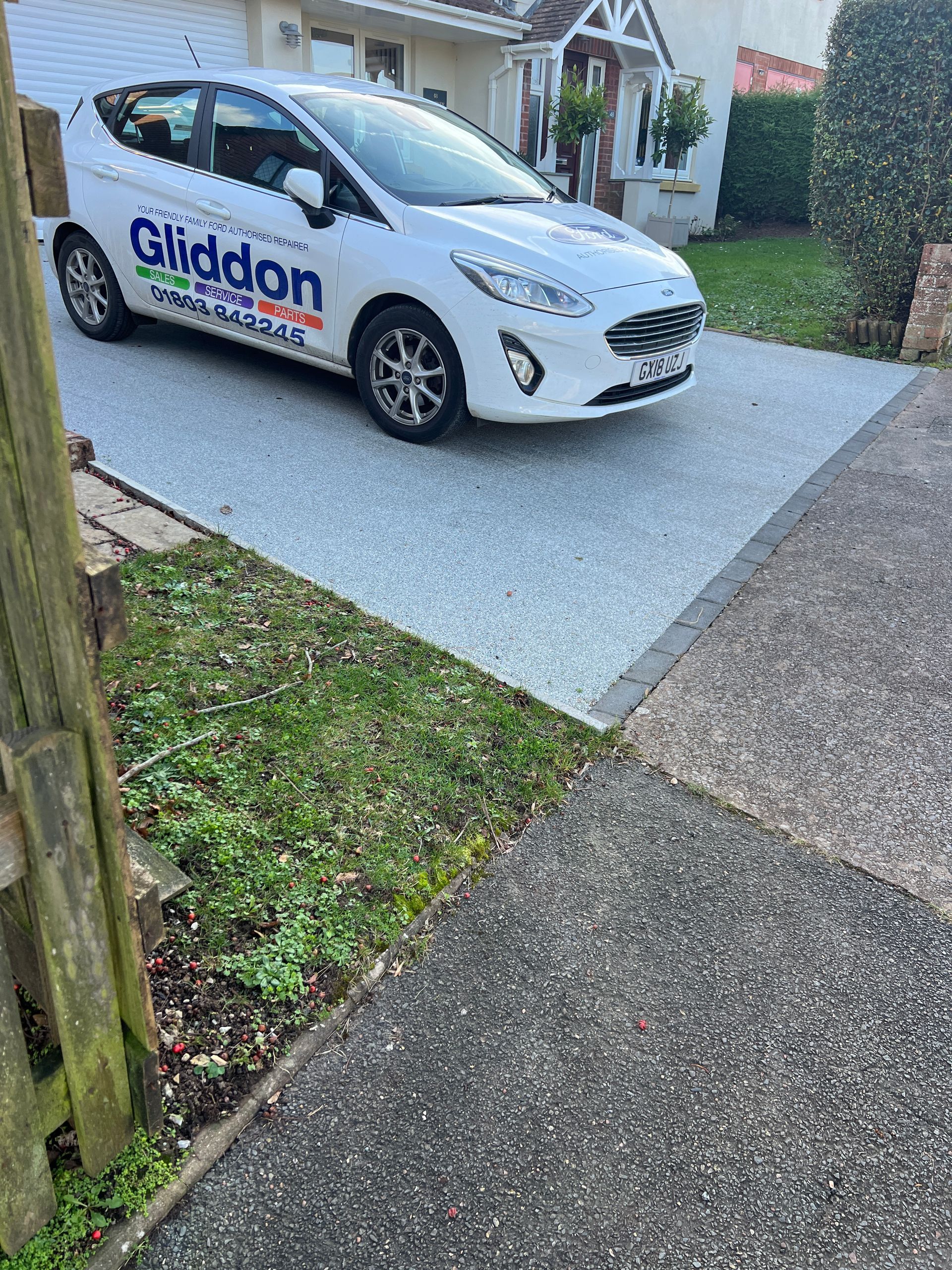 A worn out driveway attached to a brand-new light grey resin driveway with a white car parked on it.