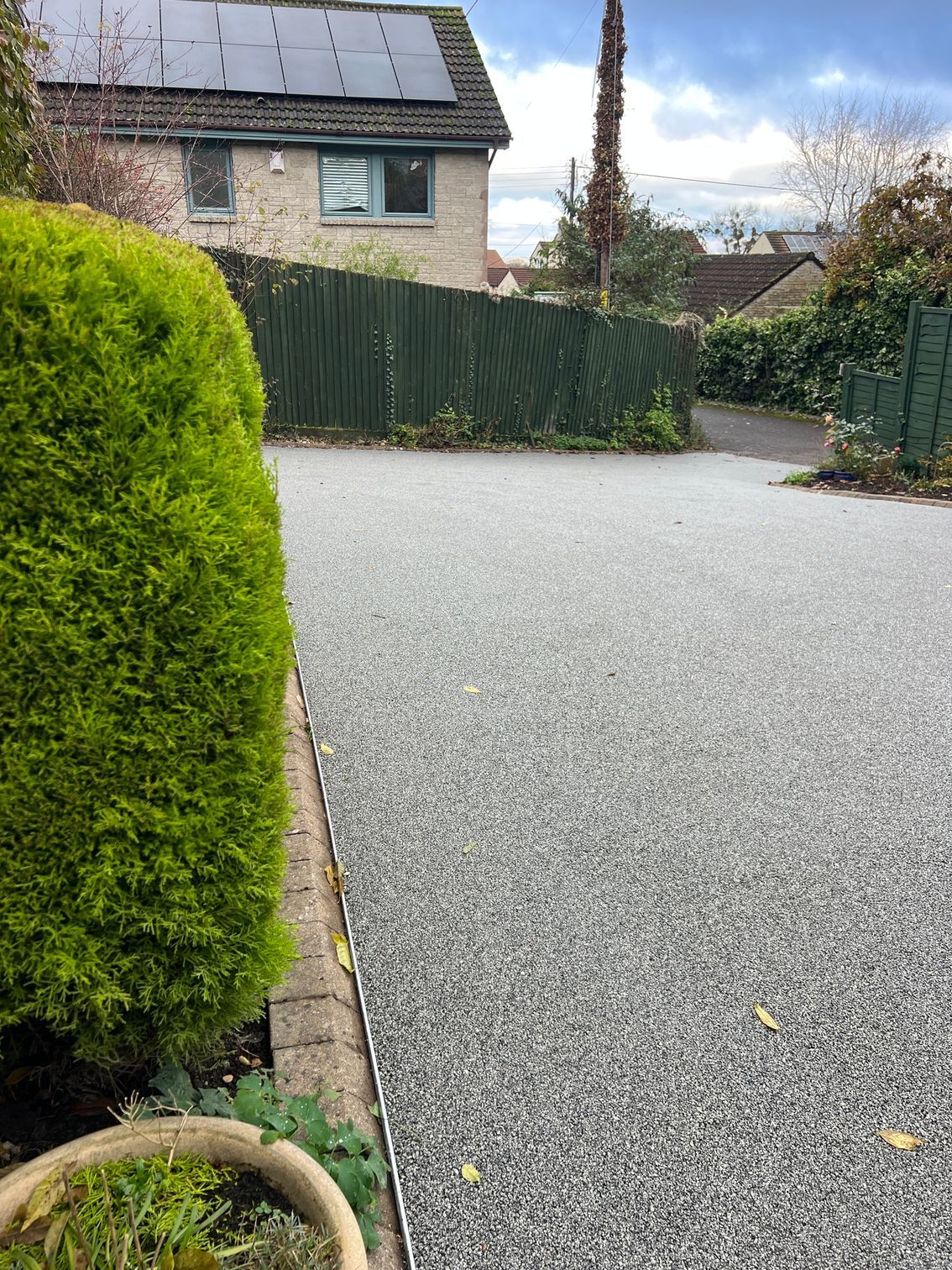 Grey resin driveway surrounded by bushes and wooden fences.