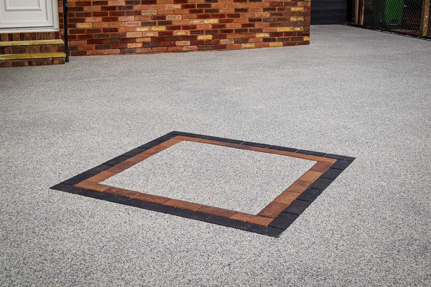 Grey resin driveways with a resin square on it, outside a red brick house.