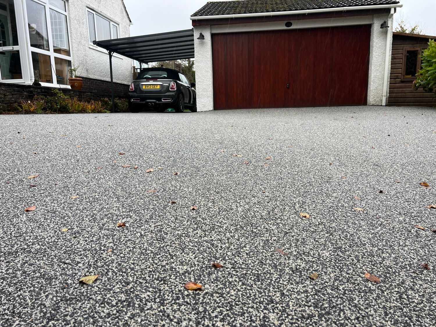 Grey resin driveway, with a brown, stained garage door in the background.