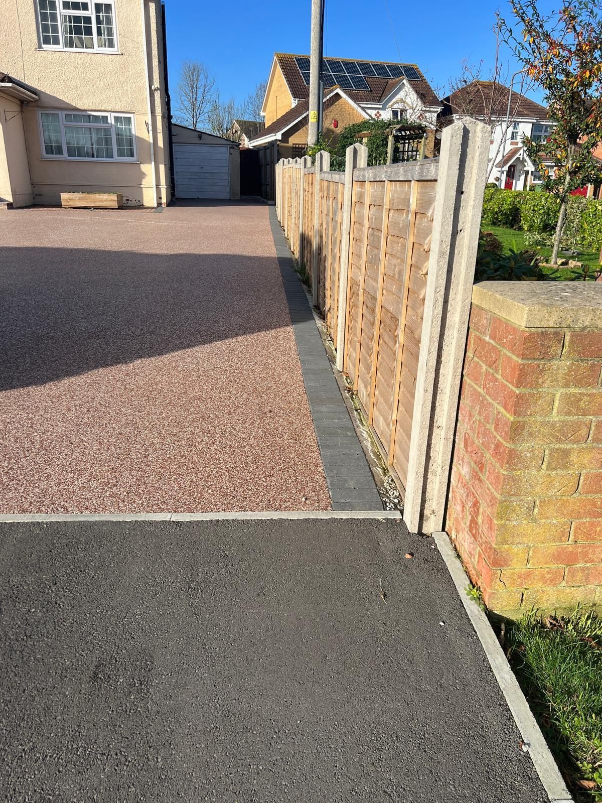 A driveway with a wooden fence and a brick wall next to a house.