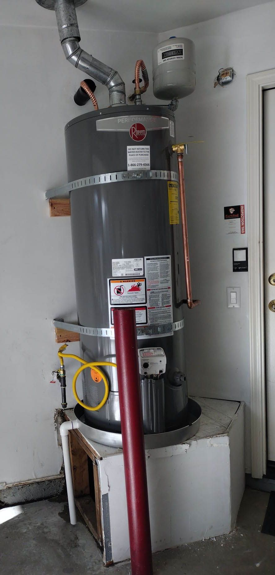 A water heater is sitting in a garage next to a door.