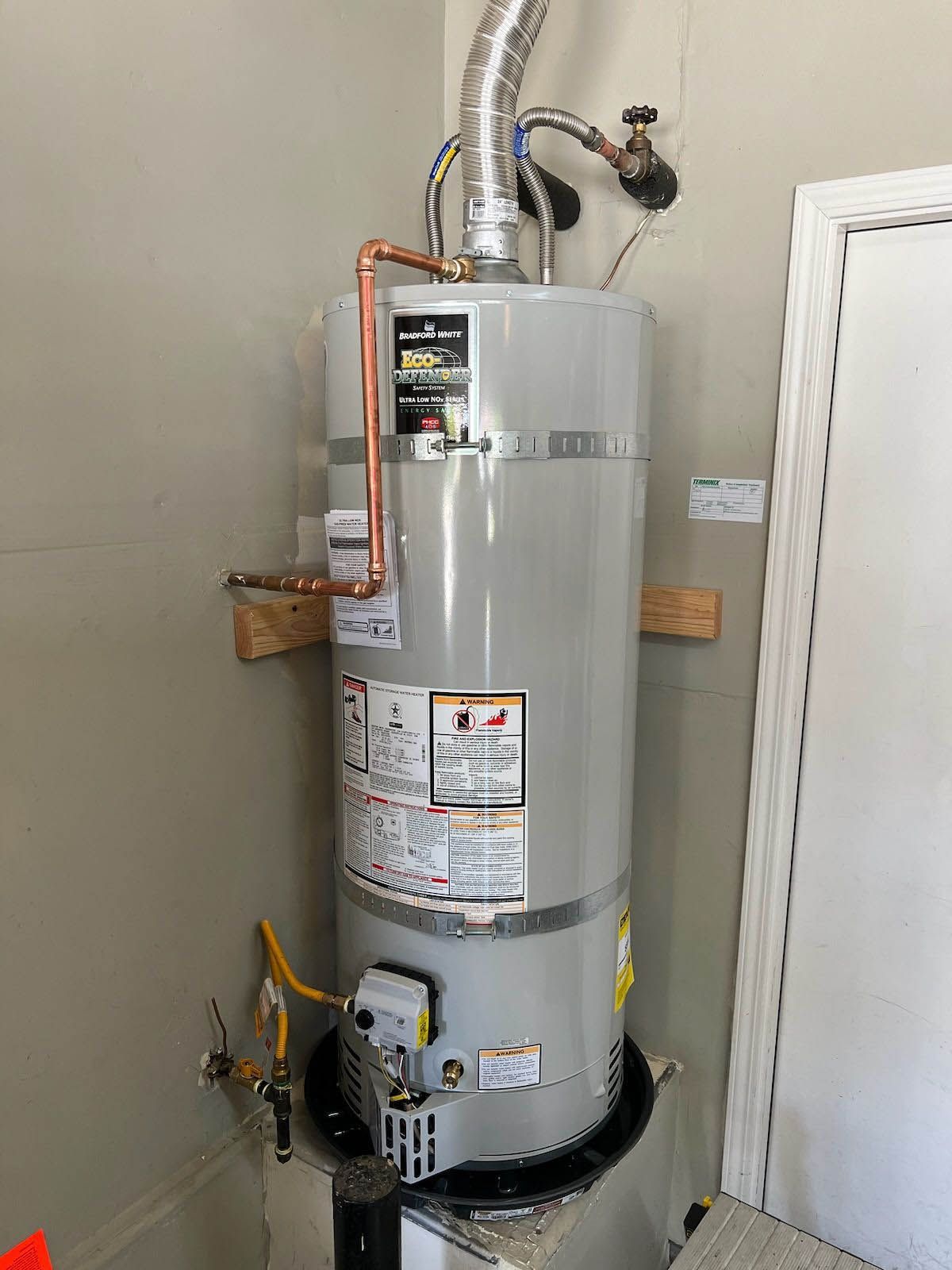 A water heater is sitting in a corner of a room next to a door.