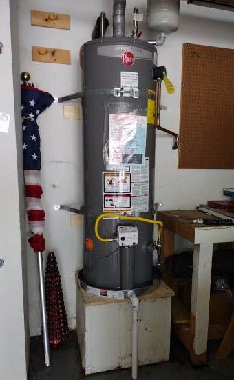 A gas water heater is sitting on top of a white box in a room.