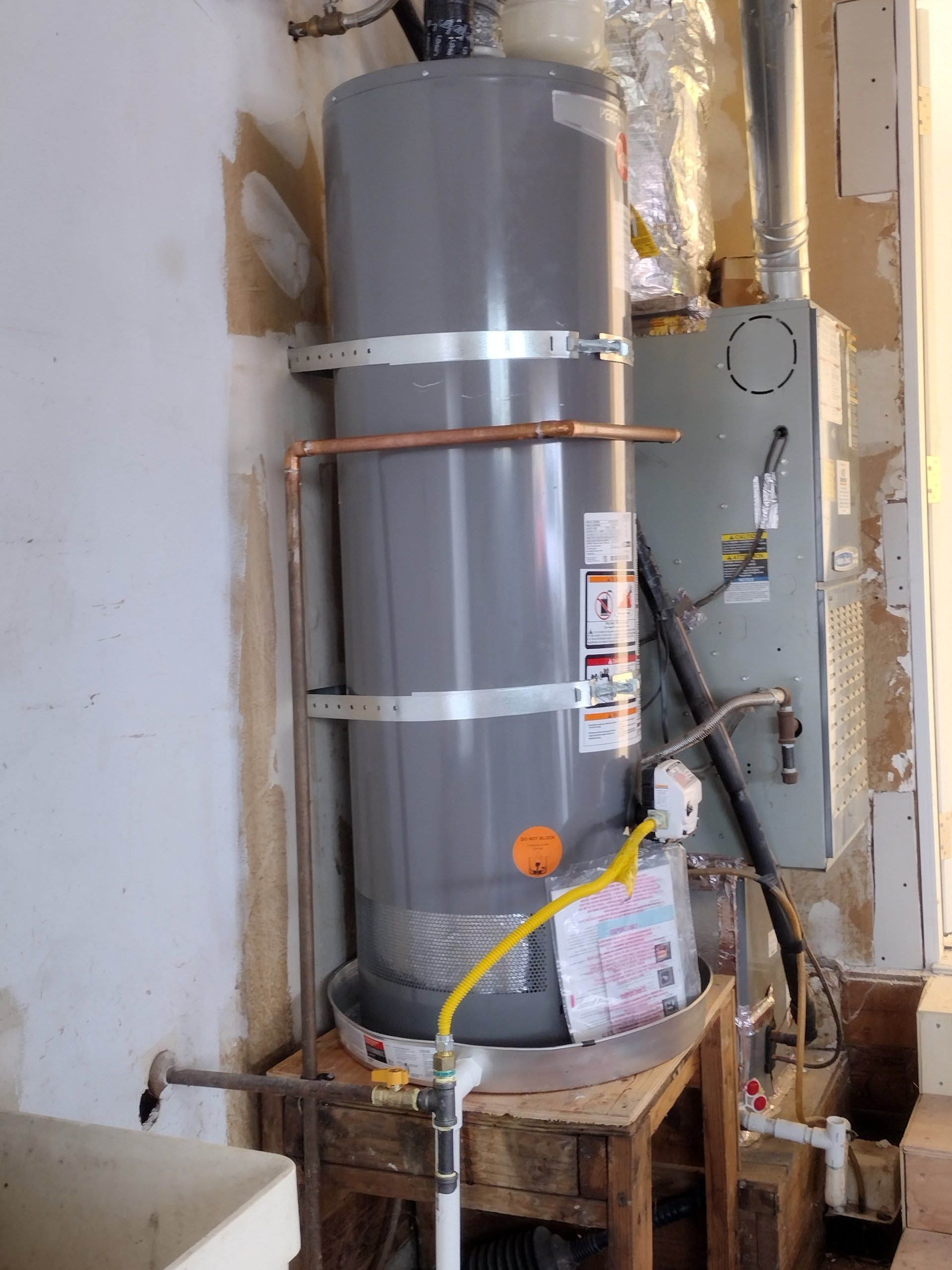 A gray water heater is sitting on a wooden stool in a room.